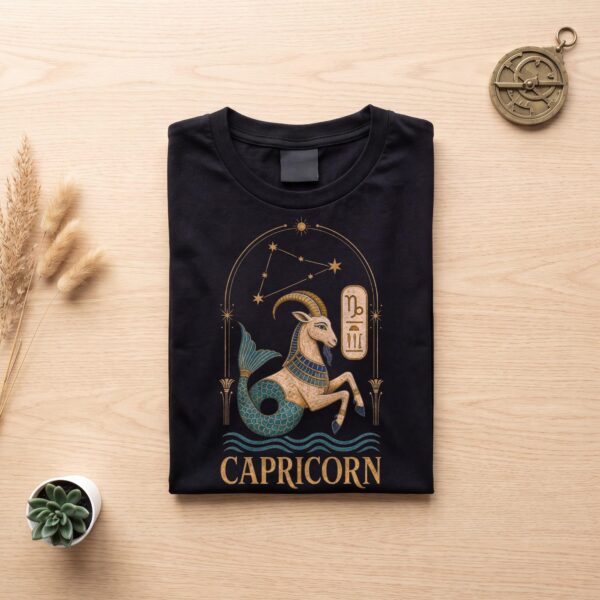 Black Capricorn Ancient Egypt zodiac T-shirt folded flat on light wood with an astrolabe