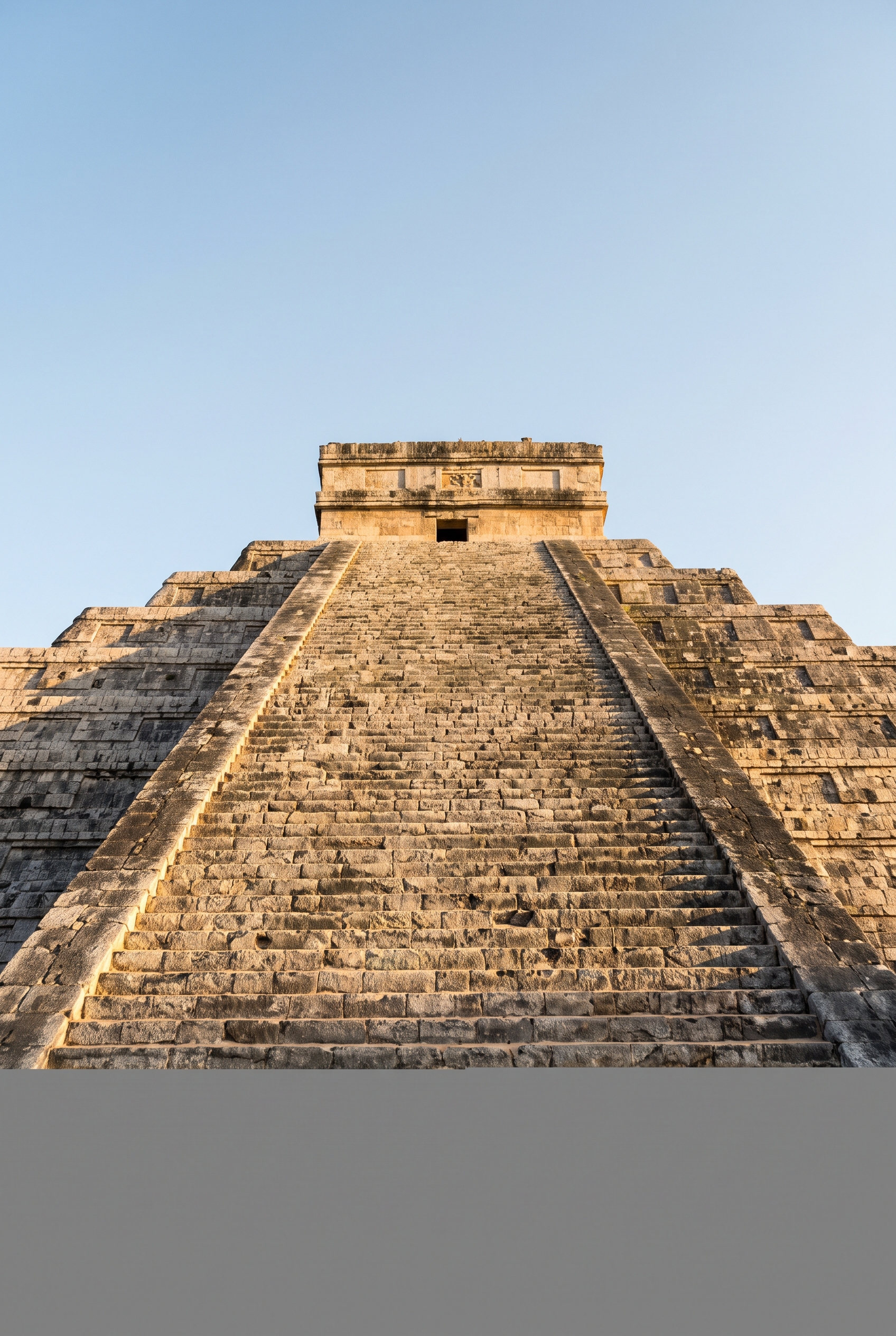 Looking up one steep stone stairway of El Castillo, its stepped terraces rising into a pale sky in golden side light