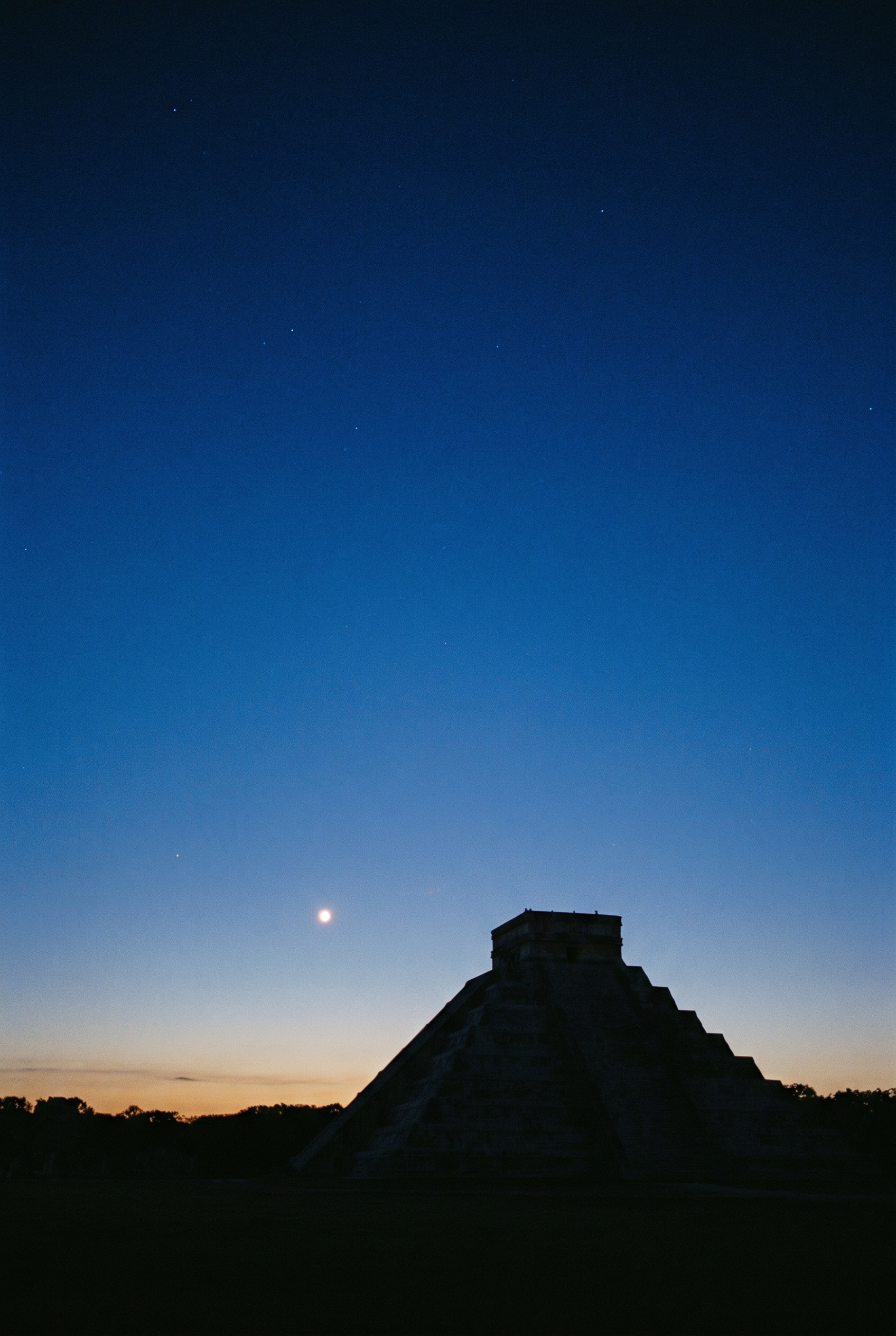 Venus blazing as the morning star low over a dark jungle horizon at first light, the silhouette of a Maya pyramid below