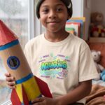 Theo · His bedroom on a rainy day, sitting by the window with a cardboard rocket he built, soft cool daylight. A cozy, indoor, giftable feel.