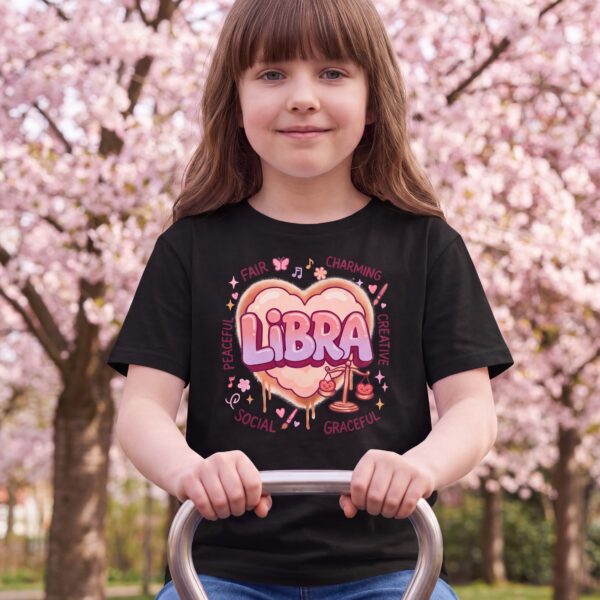 Libra Aries: Street Sign × Scorpio: Street Sign Tail Badge Youth Classic Tee (Gildan 5000B), Black, White, Sport Grey in use: A park seesaw on a bright spring day, cherry blossom trees behind, soft pink-tinted daylight.