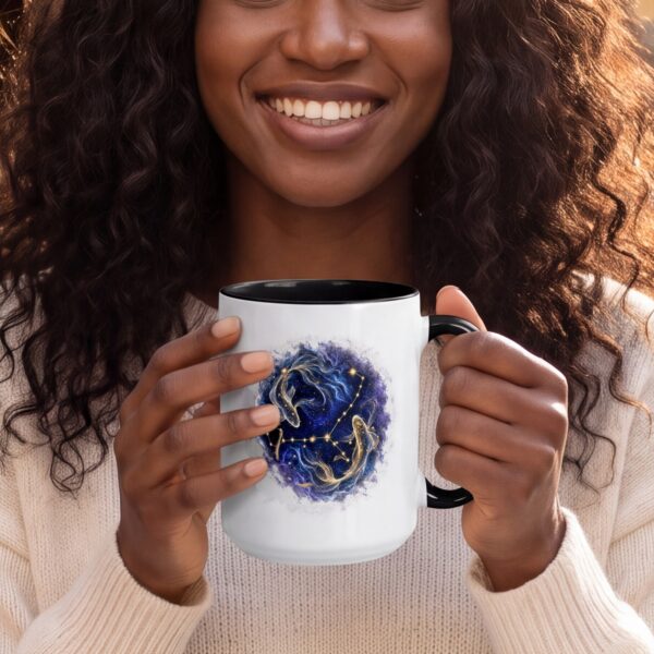 A smiling woman at an outdoor cafe holding the Pisces Celestial mug: two golden fish and the Pisces constellation in a deep blue nebula, black handle and inside